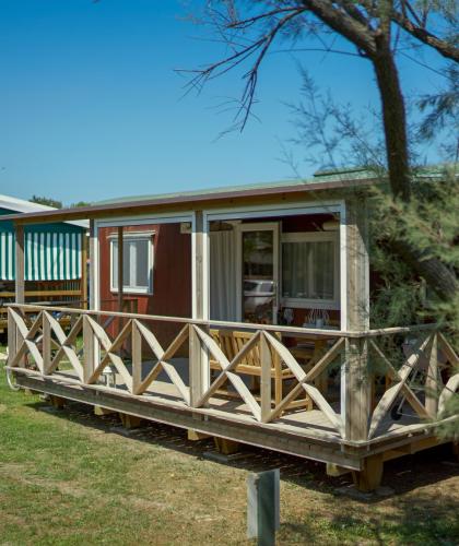 Wooden bungalow with a porch in a sunny campsite.