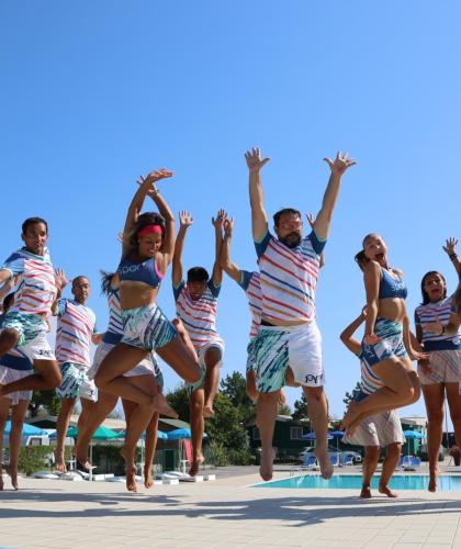 Gruppe von Menschen springt am Pool in bunten Outfits.